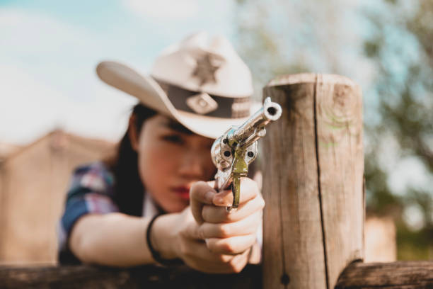 Portrait of a beautiful Chinese female cowgirl Portrait of a beautiful Chinese female cowgirl shooting with a weapon in the wild west behind a wooden fence texas shooting stock pictures, royalty-free photos & images