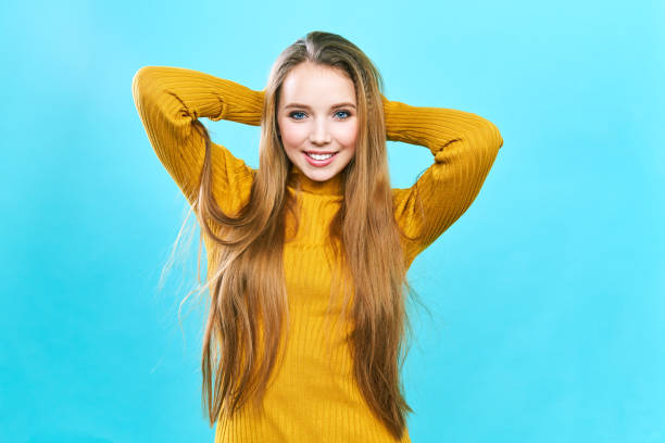 Portrait of a beautiful girl, in a yellow hat and sweater, looking at the camera and smiling cute Portrait of a beautiful girl, in a yellow hat and sweater, looking at the camera and smiling cute. On a blue background beautiful girl stock pictures, royalty-free photos & images