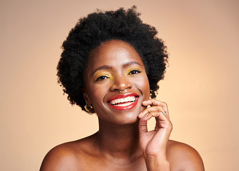 Portrait of a beautiful, smiling and happy black woman posing on a colorful studio background. Confident, trendy and cheerful female with wearing stylish makeup glowing skin and flawless complexion