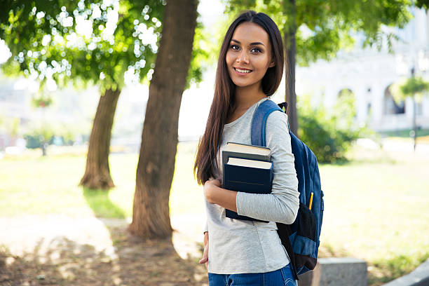 Portrait of a beautiful smiling student standing outdoors with books