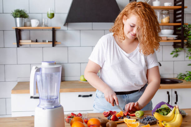 Portrait of a beautiful smiling woman preparing smoothie at home kitchen. Red head woman making smoothie. Healthy life style. fat nutrient stock pictures, royalty-free photos & images