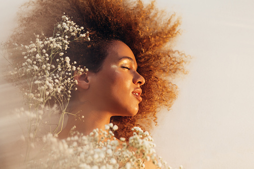 Portrait of a beautiful african american woman in white hyposphila flowers. Model woman face, perfect skin, professional make-up. Fashion Art. Background for beauty salon, treatment and spa.