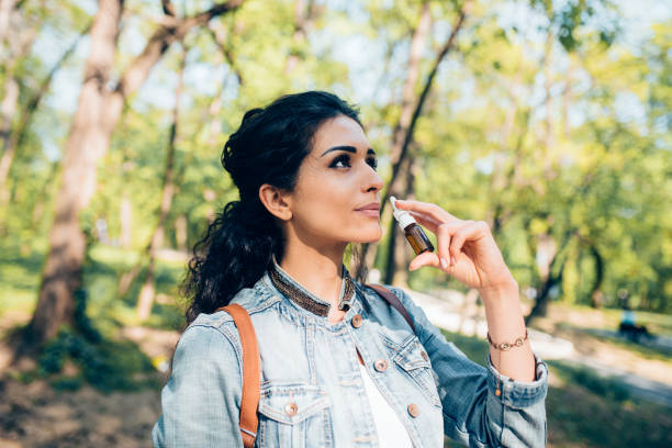 Portrait of a beautiful woman using allergy medicine outdoors Portrait of a woman using allergy medicine while walking in the park. nose spray stock pictures, royalty-free photos & images