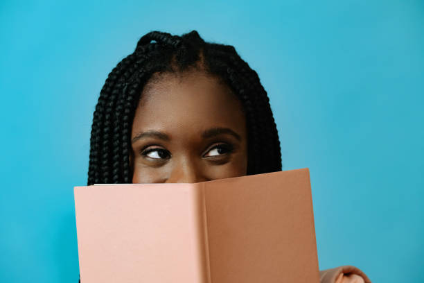 Portrait of a beautiful young african american woman with a book on a blue background looking sideways at copy space stock photo