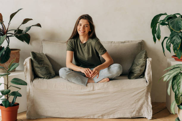 Portrait of a cheerful happy young female brunette sitting cross-legged on the sofa. stock photo