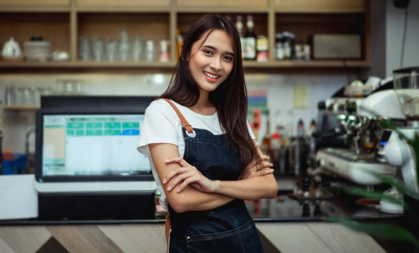 Portrait of a confident young woman standing in the doorway of a coffee shop Happy and confident smiling chinese woman, proud small business coffee shop owner standing with arms crossed behind the counter. business Malaysia stock pictures, royalty-free photos & images