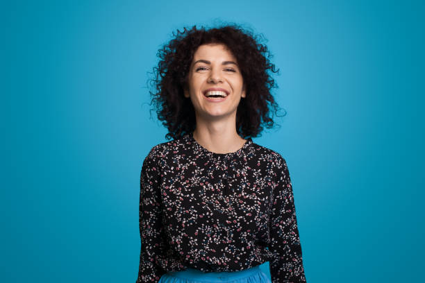 Portrait of a curly haired caucasian woman smiling isolated over blue background. Closeup portrait. Positive person. Beauty fashion model. stock photo