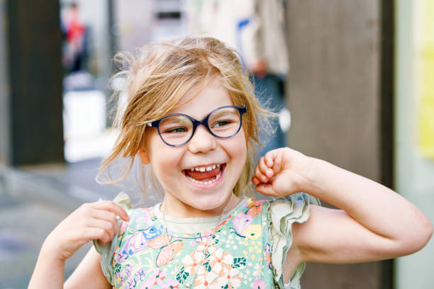 porträt eines süßen vorschulmädchens mit brille im freien. glückliches lustiges kind mit neuer blauer brille. sonniger sommertag in der stadt. - romrodinka stock-fotos und bilder