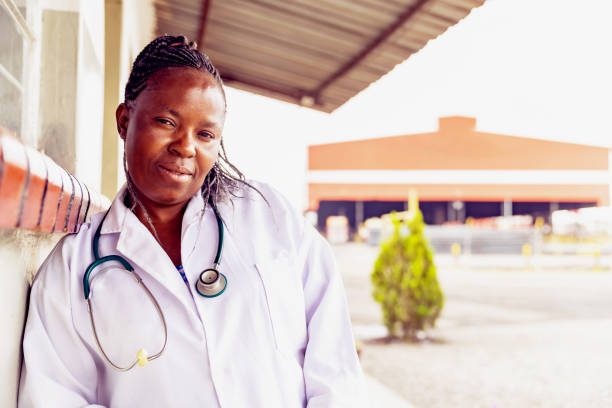 Portrait of a Female African Doctor Working for a Factory Clinic Africa, Medical, Profession - A doctor working in a factory clinic standing in front of her office and smiling at the camera for a portrait. developing countries stock pictures, royalty-free photos & images