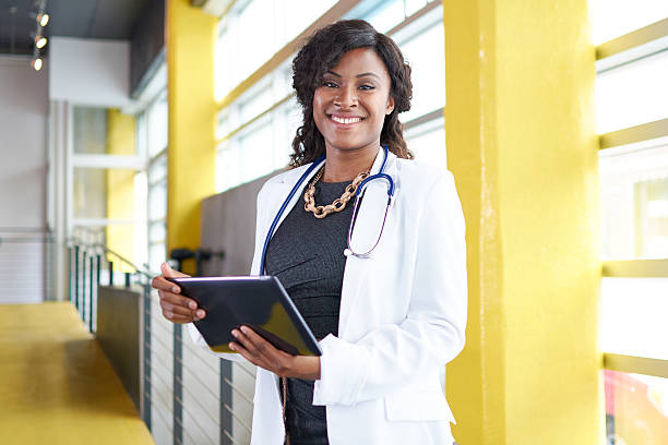 Portrait of a female doctor holding her patient chart on Friendly and attractive of a african american woman practitioner standing in a glass hall office of the clinic and examining documents director stock pictures, royalty-free photos & images