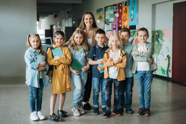 Portrait of a female teacher with students in elementary school corridor stock photo