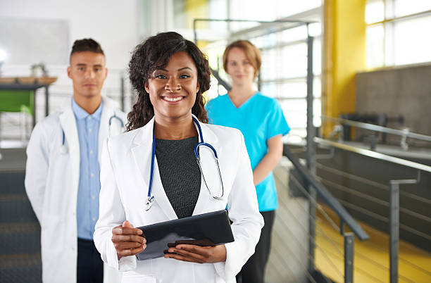 Portrait of a friendly female african american doctor and team Team of doctor and nurse hard at work to care for their patients and using technology to analyse their files and results director stock pictures, royalty-free photos & images