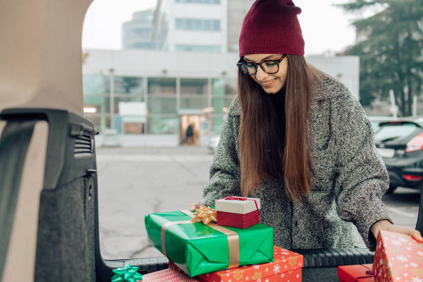porträt eines mädchens, das weihnachtsgeschenke in den kofferraum packt - auto packen für den urlaub winter stock-fotos und bilder