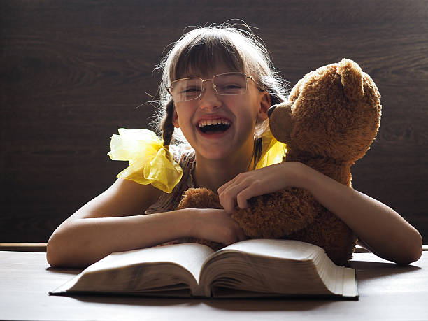 Portrait of a happy child Portrait of a happy child. Girl laughing, embracing a toy bear. Before a child is an open book. The girl yellow, large bows. Lots of sunlight. Child with glasses teddy ray stock pictures, royalty-free photos & images