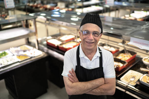 Portrait of a happy employee standing with arms crossed in front of a buffet in a self service restaurant Portrait of a happy employee standing with arms crossed in front of a buffet in a self service restaurant self service photos stock pictures, royalty-free photos & images
