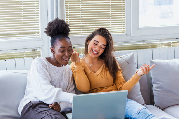Portrait of a happy girlfriends surfing the net on laptop at home. Lovable caucasian and African American girls having fun at home  surfing the net stock pictures, royalty-free photos & images