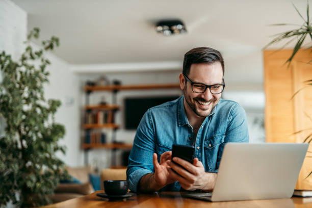 Portrait of a happy man with smart phone and laptop, indoors. Portrait of a happy man with smart phone and laptop, indoors. hot desking stock pictures, royalty-free photos & images