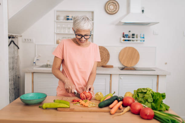 portrait of a happy senior woman chopping vegetables at her kitchen - woman chopping vegetables imagens e fotografias de stock