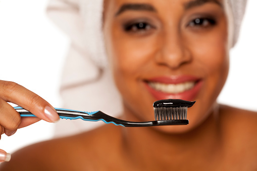 portrait of a happy young dark-skinned woman posing with toothbrush and black tooth paste on a white background