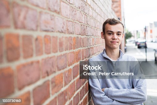 istock Portrait of a male university student with arms crossed and standing by a red brick wall in a residential street in the north of England 1333730160