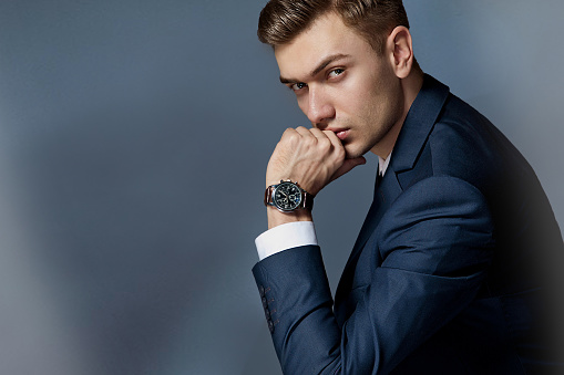 man in an expensive suit in a tie and an expensive watch posing in the studio