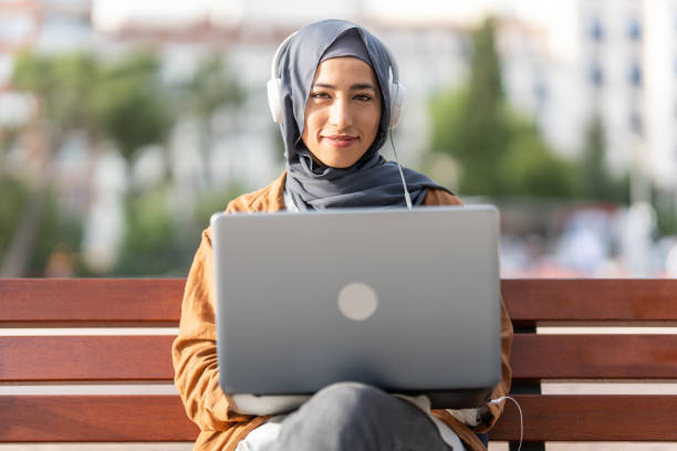 Portrait of a muslim woman using a laptop Portrait of a beauty muslim woman wearing a hijab working with a laptop in the street nomad Visa stock pictures, royalty-free photos & images