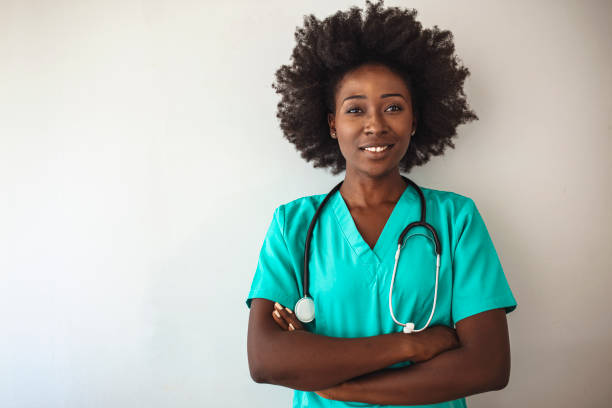 Portrait of a nurse standing in a hospita Portrait of a nurse standing in a hospital. Female nurse looking towards camera, wearing blue scrubs, arms crossed. Medical professional working in hospital. Attractive female doctor at work. female nurse stock pictures, royalty-free photos & images