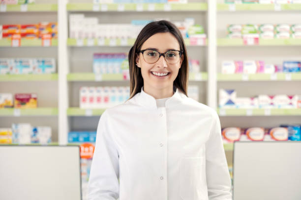 Portrait of a pharmacist in a pharmacy. A close-up shot of a pharmacist woman in uniform and with glasses standing in the middle of the pharmacy in front of a medicine shelf. Happy to do the job stock photo