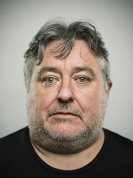 Portrait of a real english man looking at camera. Portrait of a real english man with blank expression. Vertical studio photography with sharp focus on eyes. The man has grey long hair. blank expression stock pictures, royalty-free photos & images
