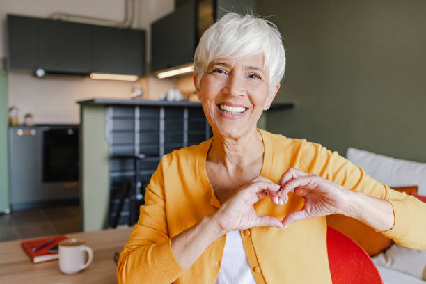 Portrait of a senior woman at home showing a heart-shaped symbol stock photo