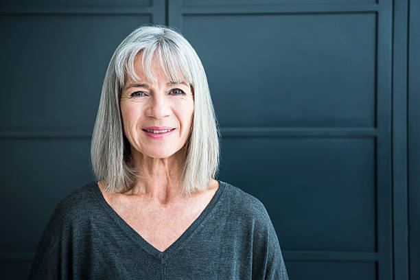 Portrait of a senior woman smiling towards camera Senior woman in her 60s with grey bobbed hair, smiling at the camera. She looks content and relaxed, in front of a grey background. bangs hair stock pictures, royalty-free photos & images