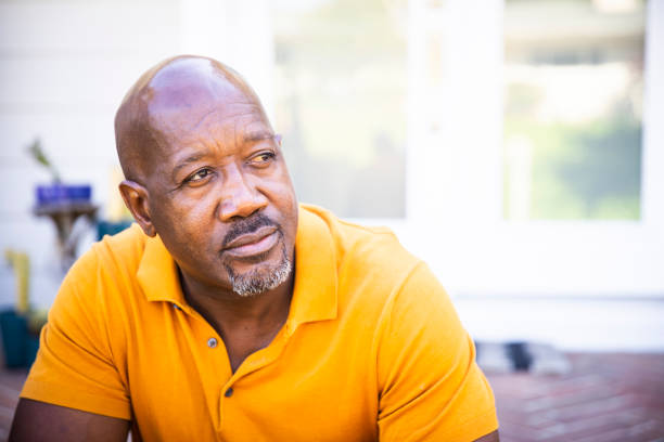 Portrait of a Serious Mature Black Man A mature black man looks out while standing on his porch sad old black man stock pictures, royalty-free photos & images