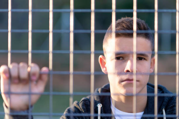 Portrait of a serious young man leaning behind a chain link fence while looking camera stock photo