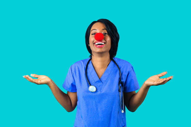 Portrait of a smiling female doctor or nurse wearing blue scrubs uniform and red nose with arms out isolated on blue background stock photo