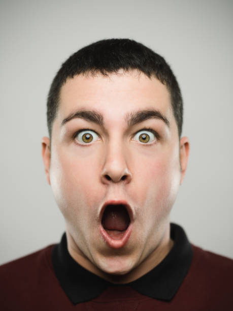 Portrait of a surprised young caucassian man looking at camera. Close-up portrait of a man with the mouth wide open and a shocked expression looking at camera. Young caucasian male with brown hair against white background. Vertical studio photography from a DSLR camera. Sharp focus on eyes. exhilaration stock pictures, royalty-free photos & images