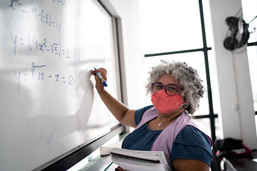 Portrait of a teacher writing in the blackboard - wearing face mask