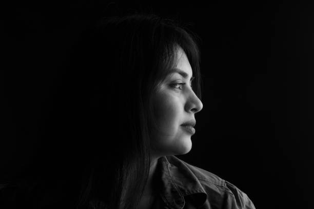 portrait of a woman side view of dark portrait of a latin woman on black background, black and white serious photos stock pictures, royalty-free photos & images
