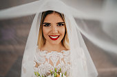 Portrait of a young bride covered with a wedding veil holding a bouquet, front view