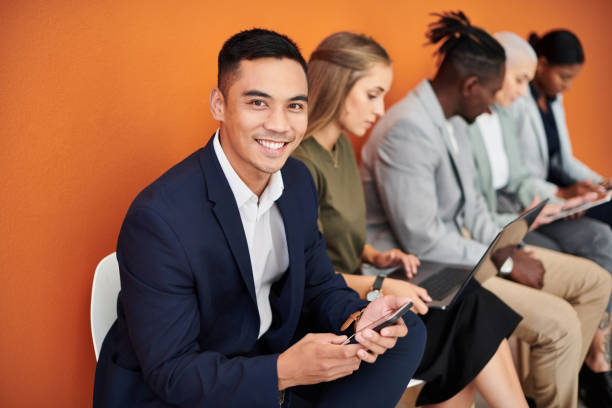 Portrait of a young businessman using a cellphone against an orange background with his colleagues in the background stock photo