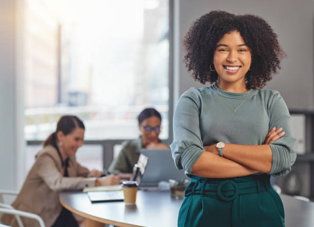 Portrait of a young businesswoman folding her arms and smiling while her colleagues have a meeting in the background stock photo