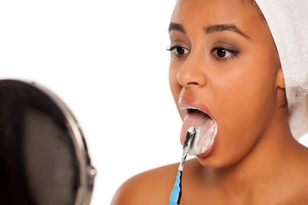 portrait of a young dark-skinned woman brushing her tongue with a toothbrush on a white background portrait of a young dark-skinned woman brushing her tongue with a toothbrush on a white background healthy tongue stock pictures, royalty-free photos & images