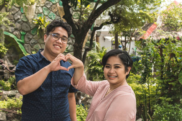 Portrait of a young Filipino couple in their late 20s make a heart sign with both of their hands. Valentines and happy relationship concepts. stock photo