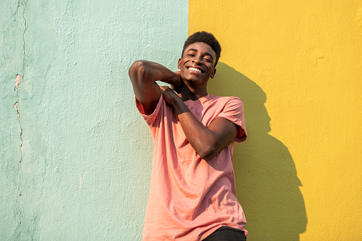Portrait of a young handsome African man looking at the camera . He is leaning on light blue/yellow wall.
