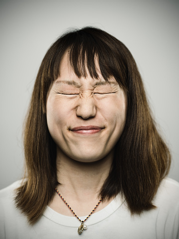 Studio portrait of a japanese young woman with closed eyes and stressed expression. The woman has around 30 years and has long hair and casual clothes. Vertical color image from a medium format digital camera. Sharp focus on eyes.