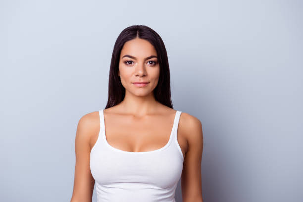 portret van een meisje van de latino-amerikaanse. ze is in een casual wit singlet staande op de zuivere licht blauwe achtergrond - borstkas stockfoto's en -beelden