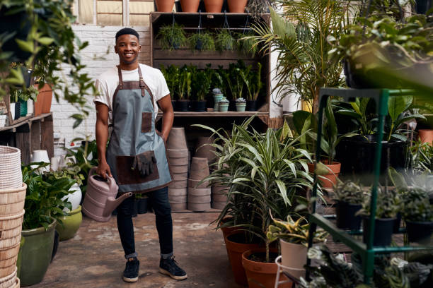 Portrait of a young man holding a watering can while working in a garden centre stock photo