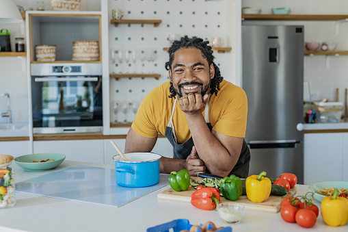 A cheerful African-American man in the kitchen surrounded by fresh vegetables