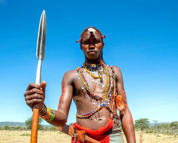 Portrait of a young Masai warrior in traditional clothing with a spear against a blue sky. Tanzania, East Africa - august 12, 2018: Portrait of a young Masai warrior in traditional clothing with a spear against a blue sky. Tanzania, East Africa, August 12, 2018. maasai warrior stock pictures, royalty-free photos & images