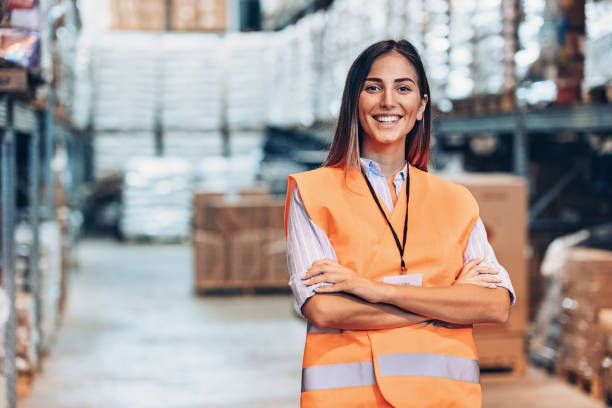 Portrait of a young woman in a warehouse Smiling young woman with reflective clothing in a large warehouse waistcoat stock pictures, royalty-free photos & images