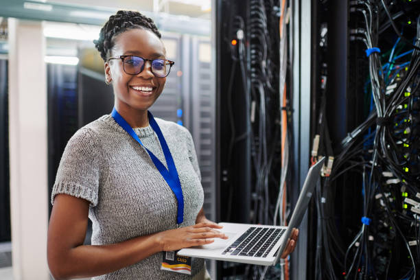 Portrait of a young woman using a laptop in a server room stock photo